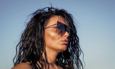 Güzel bir kadın. Moda gözlüklü şık bir kız. Dişi güneşin tadını çıkarıyor. Seksi esmer kadın uzun kıvırcık saçlı şık güneş gözlüğü takıyor ve yaz havasının tadını çıkarıyor. moda ve güzellik