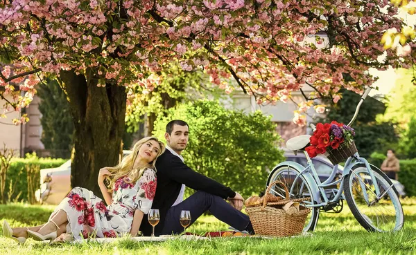 Bara kärlek kan värma oss. Romantiskt resenärspar under Sakura Blossom träd. par förälskade i grönt gräs. njuta av naturen tillsammans. ha picknick i stadsparken. man och kvinna koppla av med mat korg — Stockfoto
