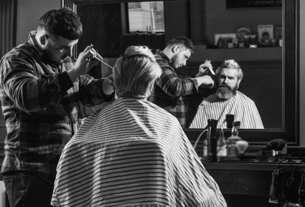 Retrato de moda del hombre. Barbería. Un joven hipster con barba cortándose el pelo en una barbería. Trabajo de peluquería profesional. Estilo de vida. maestro peluquero hace el peinado y peinado con secador — Foto de Stock