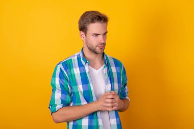 Ciddi görünüyorsun. Genç adam portresi. Yakışıklı adam sarı arka plan. Tıraşsız, kareli gömlekli.