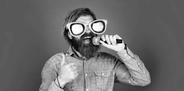Great voice. brutal caucasian hipster in party glasses. karaoke singer. unshaven guy with groomed long hair. barbershop and hairdresser. male sing music in microphone. funny bearded man with mic — Stock Photo, Image