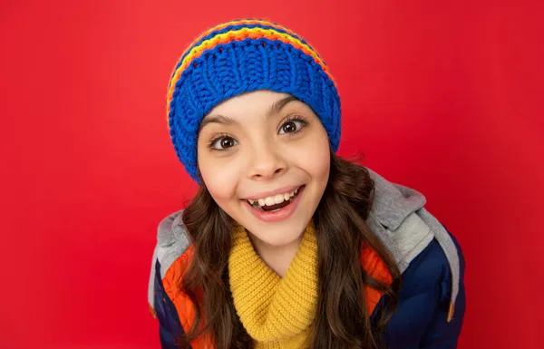 Muchacha adolescente feliz en sombrero de invierno de punto y abrigo abajo sobre fondo rojo, cara —  Fotos de Stock