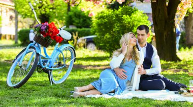 Aşk dili. Klasik bisikletli ve çiçekli romantik gezgin çift. Yeşil çimlerde birbirine aşık çiftler. Birlikte doğanın tadını çıkarıyoruz. Şehir parkında piknik yapıyoruz. Kadın ve erkek yemek sepetiyle rahatlar.