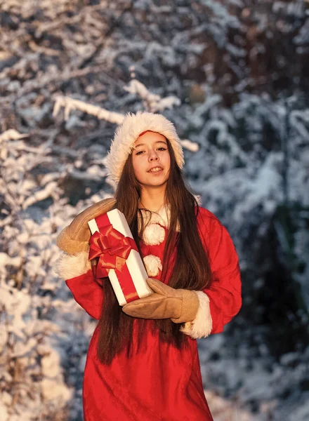 Niña pequeña en traje de santa al aire libre. Naturaleza nevada de invierno. Feliz año nuevo. niño con caja regalo de Navidad. pasar las vacaciones de invierno con alegría. regalo de Santa Claus. niña ir de compras —  Fotos de Stock