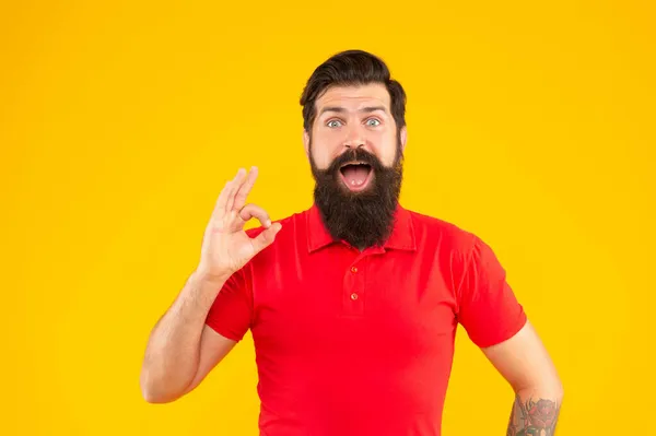 Homem barbudo espantado com bigode na tshirt mostrando gesto ok no fundo amarelo, penteado — Fotografia de Stock