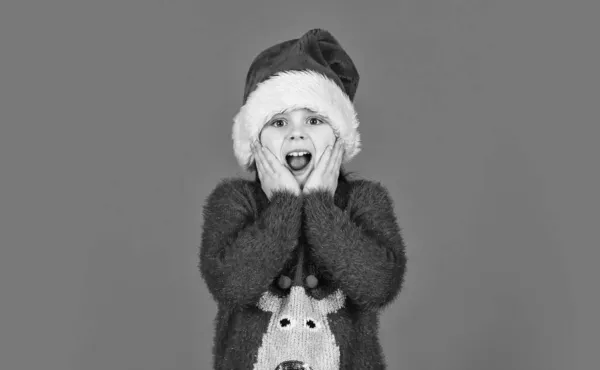 Sevimli kız Noel Baba 'nın kırmızı şapkasını giyiyor. Duygusal yüz ifadesi. Mutlu bir çocukluk. Noel 'e kadar günleri sayıyorum. Noel partisi. Duygularını zapt edemiyorsun. Noel davetiyesi — Stok fotoğraf
