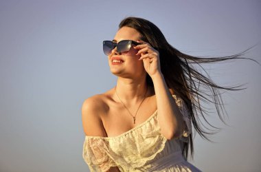 Değişim rüzgarı. Özgürlük ve uyum. Kadın psikolojisi. Güneşli mavi gökyüzünde güzel bir kadın. Yaz modası. Güneş gözlüklü kız fotokopi uzayı. Yumuşak yaz elbisesi içinde şık bir manken. Yaza doğru