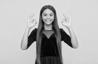 Tamam, tamam. Çocuk OK işaretlerini sarı arka planda gösteriyor. Mutlu kız mutlulukla gülümsüyor. Katılıyorum ve kabul edilebilir. Anlaşma ve izin. Her şey yolunda.