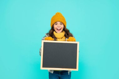Kış kıyafetleri içinde hayretler içinde genç bir kız okul karatahtasını fotokopi alanı ve reklamla tutuyor..