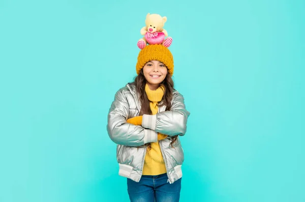 Šťastný dospívající dívka s hračka medvěd zkřížené ruce. dítě nosit teplé oblečení na modrém pozadí. — Stock fotografie