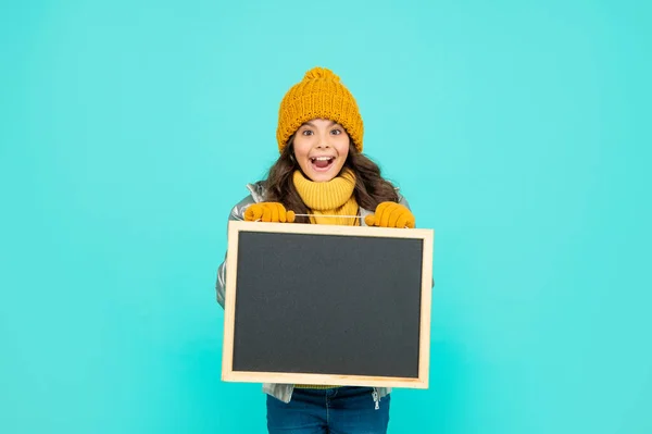 Asombrado adolescente chica en invierno ropa celebrar escuela pizarra con espacio de copia, publicidad. —  Fotos de Stock