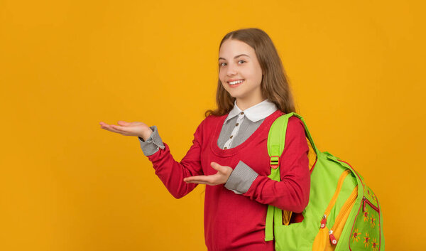 happy kid with school backpack presenting product on yellow background, back to school.