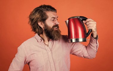 Bunu dene. Adam çay ya da kahve içecek. Bıyıklı ve sakallı vahşi bir adam. Elektrikli ev aleti. Sakallı adam kırmızı elektrikli su ısıtıcısı kullanıyor. Erkek ev idaresi konsepti. Sıcak suya ihtiyacım var.