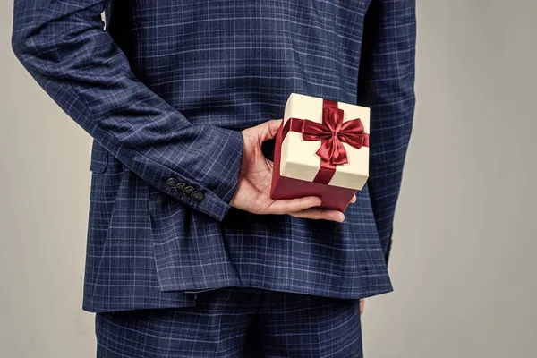 Κουτί δώρου δεμένο με κόκκινη κορδέλα φιόγκο που πραγματοποιήθηκε στο αρσενικό χέρι πίσω στην πλάτη σε επίσημο στυλ κοστούμι μόδας, παρουσιάζουν — Φωτογραφία Αρχείου