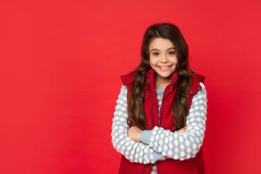 Kış mevsiminde kıvırcık saçlı gülümseyen çocuk kırmızı arka planda yelek, kopyalama alanı, kış mevsimi