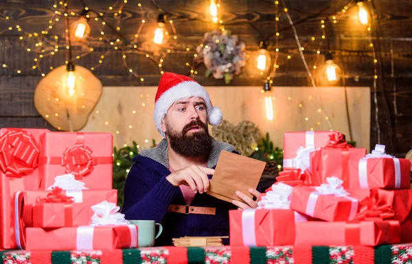 Vervul gekoesterde dromen. Vrijgevig nieuwjaar. Veel geschenken. Geschenken ingepakt met linten en strikken. Fijne wintervakantie. Een man met een bebaarde Kerstman hoed die brieven leest. Hipster bereidde geschenken voor familie voor — Stockfoto