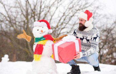Adam gülen surat, karlı doğa geçmişi. Sakallı hippi hediye kutusu. Sürpriz konsept. Kış oyunları. Kış aktivitesi. Kış tatili Adam kardan adam yaptı. Noel Baba şapkası dışarıda eğleniyor.