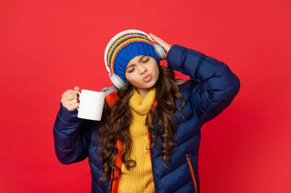 To dítě poslouchá hudbu ve sluchátkách. Ranní šálek kávy. teen dívka v kabátu pití čaje. — Stock fotografie