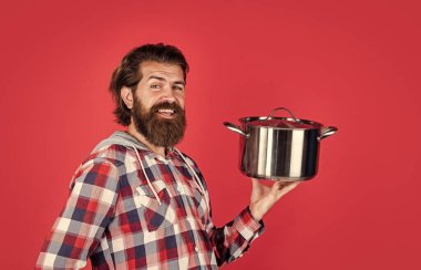 Kareli gömlekli, olgun, yakışıklı bir adam yemek pişirmek için tava tutuyor.