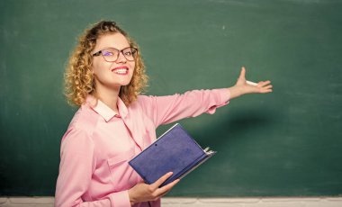 Pedagog kitabı tutuyor ve bilgiyi açıklıyor. Öğretmen zor konuyu açıkla. Karatahtanın önündeki kadın öğretmen. Öğrencilerin en iyi öğretmeni. Bilgiye karşı tutkulu. Eğitim kavramı