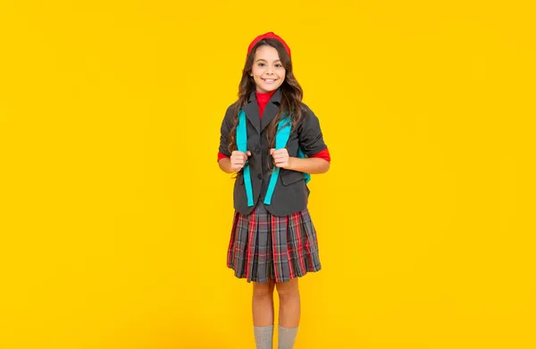 Щаслива дівчина-підліток у формі зі шкільною сумкою на жовтому фоні, школа — стокове фото