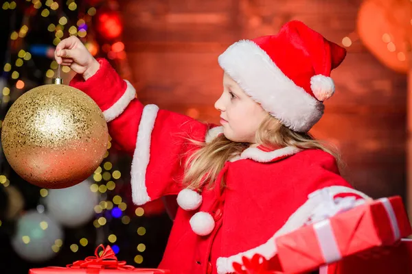 Deze prachtige gouden bal ornament zal u vullen met kerstsfeer. Klein meisje dat naar versierbal kijkt. Schattig kind met kerstbal. Klein kind met kerst glitter bal — Stockfoto
