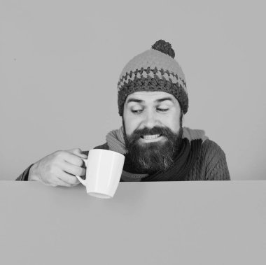 Sıcak şapkalı adam turuncu arka planda beyaz bardak tutuyor.