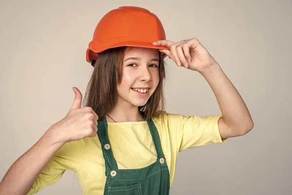 Allegra ragazza adolescente in uniforme da lavoro e casco spettacolo pollice in su, ingegnere — Foto Stock