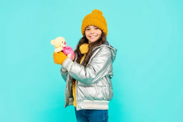 Sorrindo adolescente menina segurar brinquedo urso. criança vestindo roupas quentes no fundo azul. — Fotografia de Stock