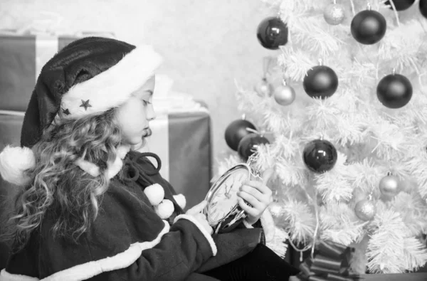 В ожидании чуда. Новогодний отсчет. Девочка в шляпе Санта держать часы взволнованные счастливое лицо подсчет времени до нового года. Новый план на последнюю минуту. Счастливого Рождества. Последняя минута до полуночи — стоковое фото