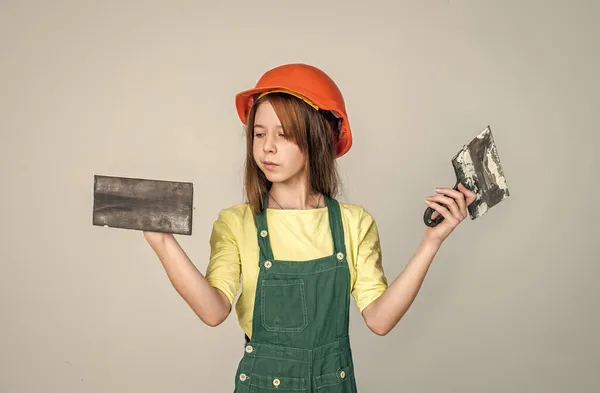 Kezdjük. felújítás és javítás. munkaeszközzel. Tini lány sisakban és boilersuit spatulával. A gyerek keménykalapot visel. Gyereképítő az építkezésen. Munkás mérnök. építész műhelyben — Stock Fotó