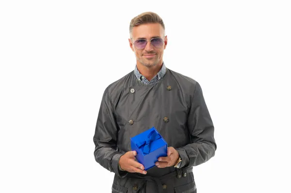 Glücklich schöner Mann im lässigen Trenchcoat hält blaue Geschenkschachtel isoliert auf weiß, Geschenk — Stockfoto