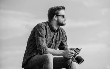Adam açık havada gökyüzü arka planında. Antika ekipmanlar. Gazeteci fotoğraf çekiyor. Hippi fotoğrafçı. Blogger video blogu çekiyor. Yakışıklı blogcu, gezgin, geçmişe dönük kamera. Elle ayarlar. Seyahat blogçusu