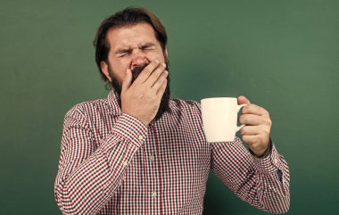 Esneyen adam yeşil arka planda fincandan sabah kahvesi içiyor, uykusuzluk.