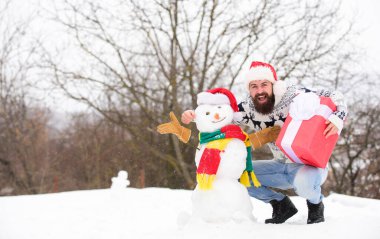 Açık havada sakallı hippi. Kış oyunları. Kış aktivitesi. Kış tatili Adam kardan adam yaptı. Noel Baba şapkalı adam dışarıda eğleniyor. Eğlence ve eğlence. Adam gülen surat, karlı doğa geçmişi