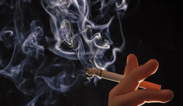 Dym i duszenie. Ciemne tło dymu papierosowego. Płonący papieros w męskiej dłoni — Zdjęcie stockowe