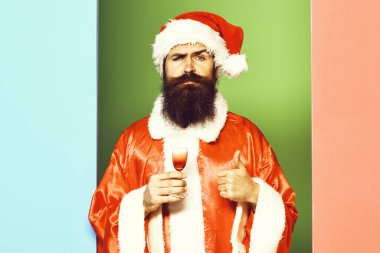 Yakışıklı, sakallı, uzun sakallı, ciddi sakallı Noel Baba. Elinde kırmızı noel ya da yılbaşı ceketi ve renkli stüdyo şapkası olan alkolik bardakları var.