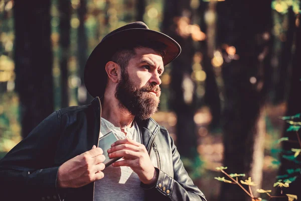 Tipo brutal barbudo vaquero beber alcohol matraz de metal. Hipster con barba beber alcohol naturaleza fondo desenfocado. Camping de senderismo. Concepto vagabundo. Bebida alcohólica. Hombre nómada llevar alcohol con él —  Fotos de Stock