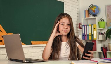 Çocuk öğrenci masaya otur ve bilgisayar kullan. Kız üniversite öğrencisi. Okula dönüyorum. Genç kız sınıfta dizüstü bilgisayarla çalışıyor. Neşeli çocuk internetten konuyu öğreniyor. Modern eğitim. bilgi günü