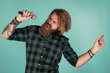 Mikrofonlu erkek şarkıcı. Karaoke konsepti. Kareli gömlekli sakallı adam şarkı söylüyor. Sıradan bir adam şarkı söylerken insani duygularını ifade eder. Mikrofonlu duygusal hipster. Meleklerin dili.