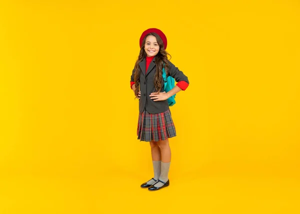 Chica adolescente sonriente en uniforme y boina con bolsa de escuela sobre fondo amarillo, moda escolar — Foto de Stock