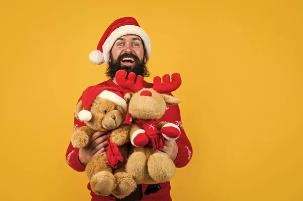Brutal skäggig kille i Santa claus hatt och tröja med leksaker på julafton, jul leksaker — Stockfoto
