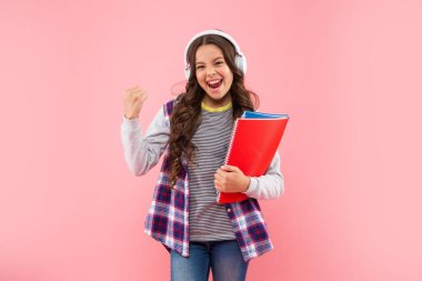 Başarılı çocuk, kulaklıkla müzik dinle. Pembe arka plan ve bilgi üzerine çalışma kitabı tut.