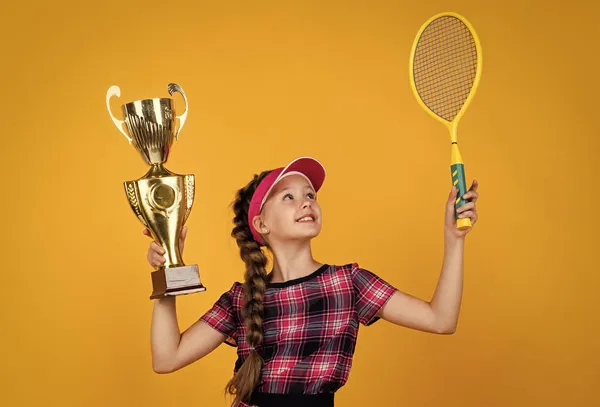 Győztes gyermek ütővel és bajnoki kupával. A tini lány megnyeri a tenisz bajnokságot. sport. teniszező vagy tollaslabda játékos. egészséges és aktív életmód. Tele energiával. Boldog gyermekkort. gyerek hold ütő — Stock Fotó