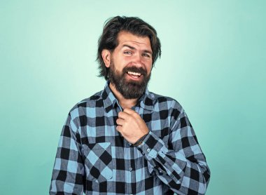 Vahşi sakallı hippi. Bıyıklı, olgun bir adam. İnsan duygularını ifade etmek. Kareli gömlekli mutlu adam. duygusal adam mavi arka planda