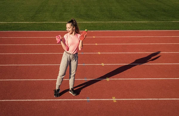 Treinamento menina adolescente com halteres e garrafa de água no estádio ao ar livre, fitness — Fotografia de Stock