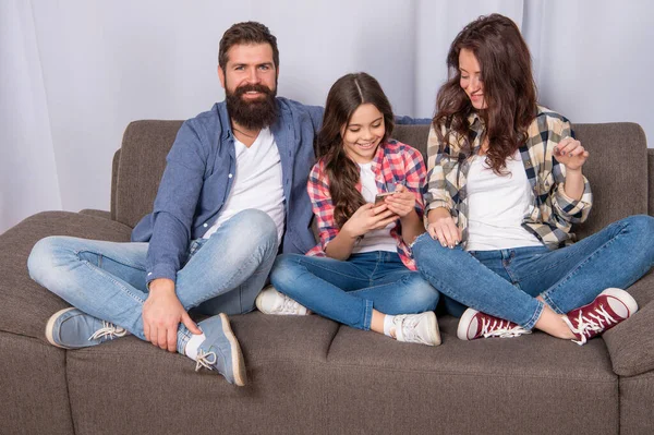 Menina feliz criança mensagens no smartphone sentado ao lado de pai e mãe no sofá, família — Fotografia de Stock