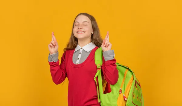 Criança feliz com escola mochila cruz dedos fazendo desejo no fundo amarelo, de volta à escola — Fotografia de Stock