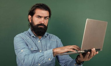 Bilgisayarda çalışan olgun bir öğretmen. Sınıfta dizüstü bilgisayarlı kaba sakallı bir adam çalışıyor. Online sınav için hazırlanın. Özel ders üzerine üniversite hocası. Okula dönüyorum. çevrimiçi kayıtdışı eğitim