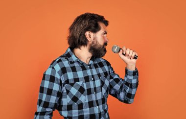 Etkinlik yöneticisi. Mikrofonlu adam. Müzik konsepti. Kareli gömlek giyen şarkı söyleyen adam. Karaoke kulübünde kendine güvenen bir erkek şarkıcı. Parti performansı. Sakallı hippi mikrofonda şarkı söylüyor.